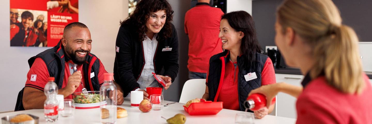 Vier Verkaufsmitarbeiter von Kaufland gut gelaunt bei der Mittagspause im Pausenraum der Filiale.
