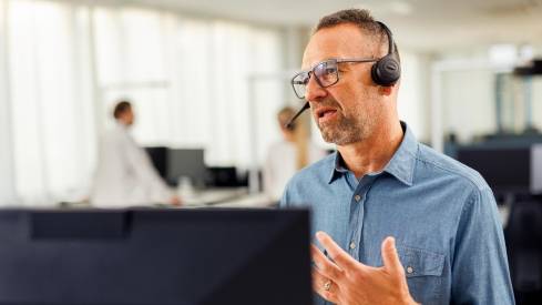 Kaufland-Mitarbeiter mit Headset vor einem Bildschirm in angeregtem Gespräch bei einer Telko.