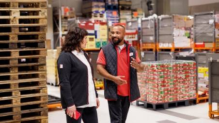 Im Filiallager: Kaufland-Verkaufsmitarbeiter im Gespräch mit einer Kollegin. Im Hintergrund ein Stapel Paletten.